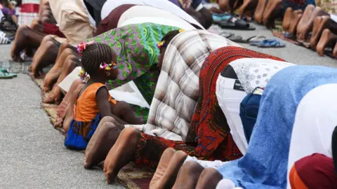 AFP A little girl sits next to people praying at the site of a bus terminal in Adjame, a quarter of Abidjan, on June 14, 2018