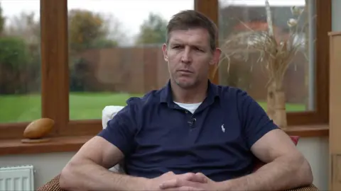 Dafydd in a blue polo shirt sitting in a chair by the window with garden visible