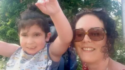 cohen's genetic journey 6 year old boy with dark brown hair waving his arms, next to mum with curly brown hair wearing sunglasses