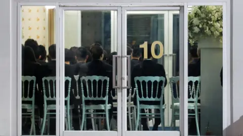 Reuters People are seen through a glass door as they attend a funeral of Vichai Srivaddhanaprabha in Bangkok