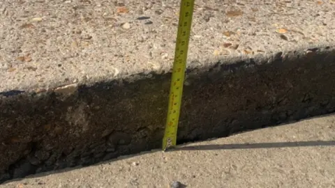 Charlie Mann Tape measure showing the concrete road surface on Miles Gray Road in Basildon has dropped by 4in (10cm)