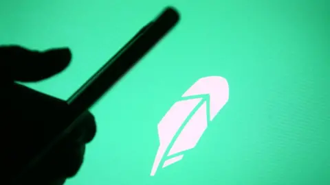 Getty Images Robinhood app logo with a silhouette of a hand using the phone