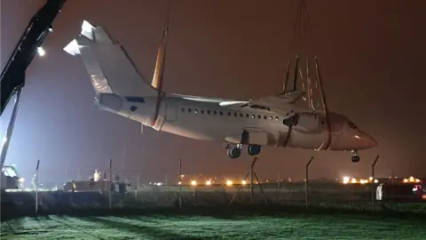 BBC Avro RJ85 being lifted over road by cranes