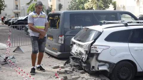 EPA An Israeli man inspects damage to a car caused by a rocket fired from Gaza (9 August 2018)