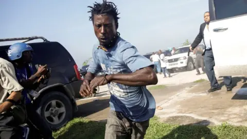 Reuters People run as Senator Jean-Marie Ralph Féthière fires a gun in the air