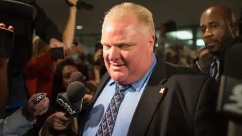 Getty Images This file photo taken on 15 November 2013 shows former Toronto Mayor Rob Ford surrounded by the media as he leaves his office at Toronto City Hall.