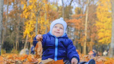 Getty Images small child in warm clothes playing in fallen autumn leaves