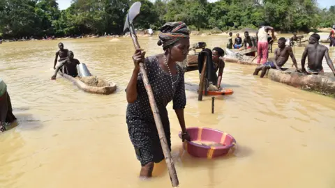 AFP Gold prospectors work in the Pampana river on March 5, 2018 near Mekeni, northern Sierra Leone. Down a dirt road that slopes off a bridge, hundreds of men and women waist-deep in the river sift through gravel, separating specks of gold from the sludge. It may be the eve of a general election in Sierra Leone, but those who eke out a living here in Magburaka have few expectations from a new government, whichever party wins