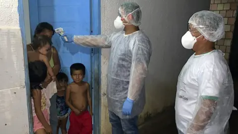 AFP Handout photo released by the Special Secretariat for Indigenous Health (Sesai) showing a worker checking the temperature of members of the Tikuna group in Lago Grande, Amazonas state, Brazil (2 April 2020)
