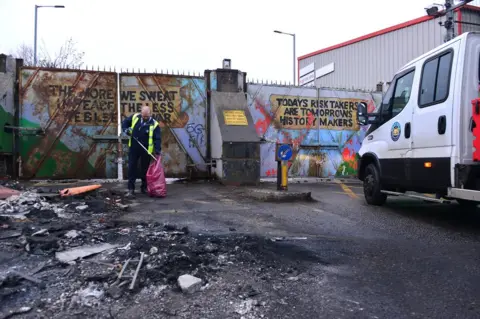 Pacemaker A council worker clears debris from a road on which rioting took place in west Belfast