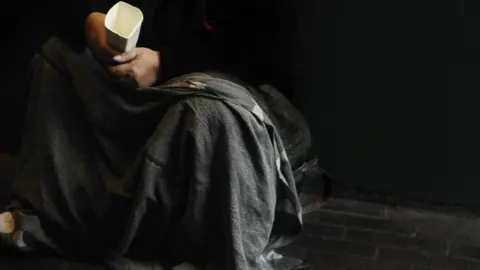 PA Media Man holding a cup for spare change