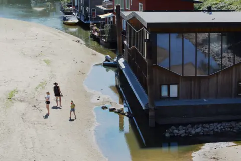 Getty Images People walk near boat houses on the banks of the Waal River on August 10, 2022 in Nijmegen, Netherlands.