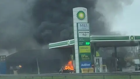 Sarah Merritt Plumes of black smoke coming from a car and its bonnet appears to be on fire