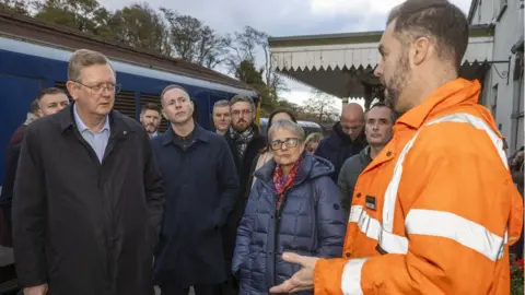 PA Media Lord Caine listens to County Down Railway chairman Robert Gardiner about the damaged caused by the flooding in Downpatrick last week