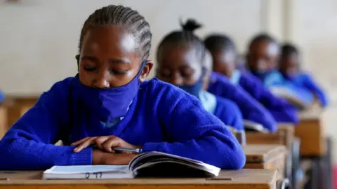 Reuters A schoolgirl wears a face mask as she reads a book inside a classroom at the Olympic Primary School during the partial reopening of schools, after the government scrapped plans to cancel the academic year due to the coronavirus disease (COVID-19) pandemic, in Kibera slums of Nairobi, Kenya October 12, 2020.