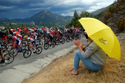Stephane Mahe / Reuters A woman holds an umbrella and watches professional cyclists cycle past