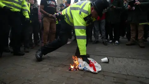 PA A police officer extinguishes a flag that was set alight by pro-Brexit protestors outside the Houses of Parliament