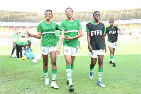 Getty Images Female footballers smiling on the pitch wearing the Nigerian kit.