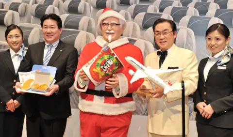 Getty Images Japan Airlines President Yoshiharu Ueki (2nd L) and Masao Watanabe (2nd R), President of KFC Japan pose with a statue of Colonel Sanders (C) wearing a Santa Claus costume at a press conference to announce plans to offer in flight KFC for 3 months from December 2012