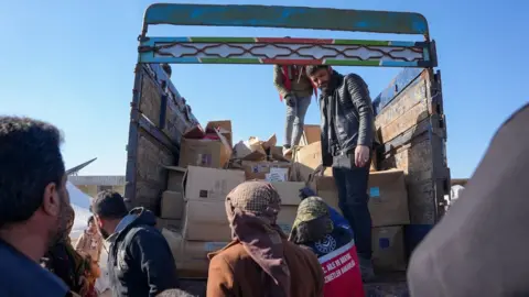 AFP File photo showing Syrians receiving aid at a make-shift shelter near the opposition-held town of Jindayris (9 February 2023)