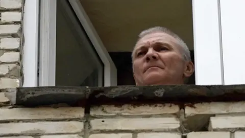 Alexei Moskalev appears at a window of the building where he is being held under house arrest