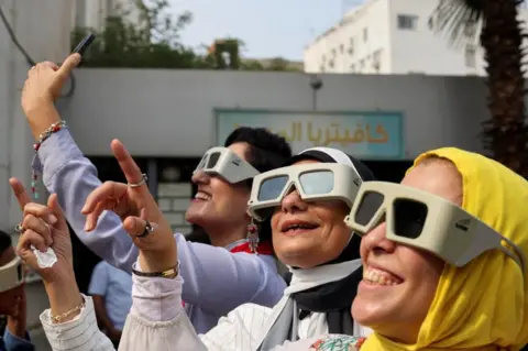 Reuters Women wearing chunky white glasses pointing up to the sky and smiling.