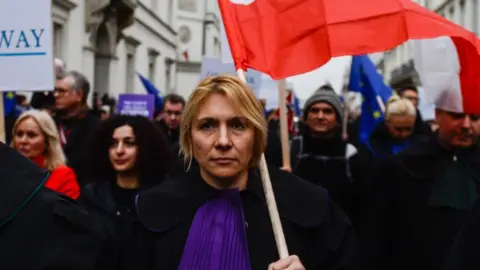 Getty Images A judge holds a Polish flag during a march against judicial reforms in Warsaw on 11 January 2020.