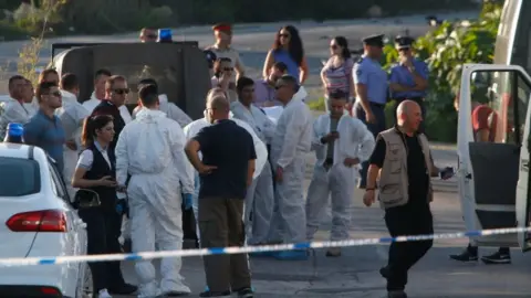 Reuters Police and forensics experts stand behind a road block after a powerful bomb blew up a car killing investigative journalist Daphne Caruana Galizia in Bidnija, Malta, 16 October 2017