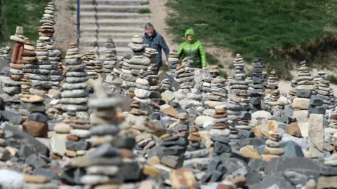 Owen Humphreys/PA Media People walk by pebble stacks