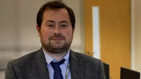 Tomi Rowlands in a suit and tie standing in an office