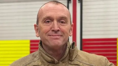 A man in fire uniform smiles at the camera