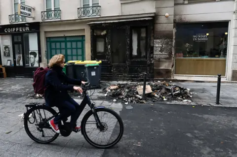 YVES HERMAN/reuters A cyclist rides her bicycle past a burnt store and damage in a street the day after clashes during protests over French government's pension reform in Paris, France, March 24, 2023.