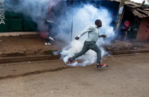 Donwilson Odhiambo/Getty Images Man running with smoke from teargas surrounding him.