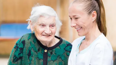 Getty Images An elderly lady with a helper