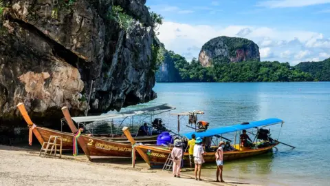 Getty Images Beautiful Thai beach with boats and tourism staff.