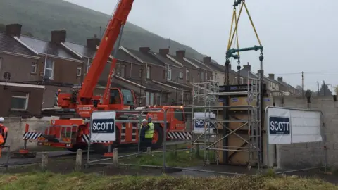 A crane begins to lift the wall away