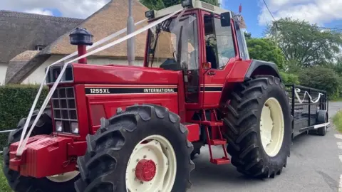 Red tractor and trailer decorated with white wedding ribbons