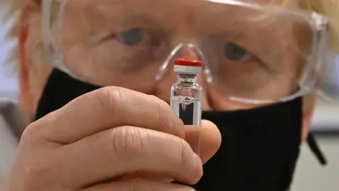 PA Media Boris Johnson holds up a vial of vaccine