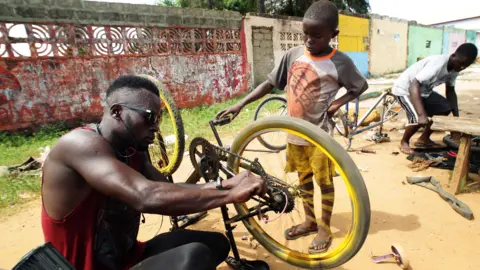 EPA Odixco F Gongoar, owner of God Bless Bicycle Repair Center, repairs a bicycle as a trainee looks on in Paynesville, Liberia - Monday 24 May 2021