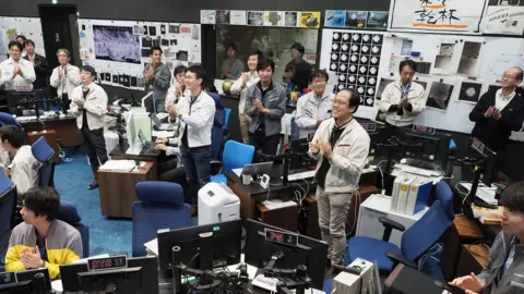 Jaxa/AFP Jaxa scientists and staff smile and clap their hands from mission control