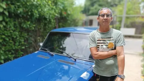 Jorge Lloro stands by blue car