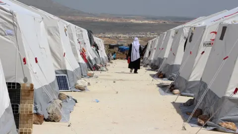 AFP A Syrian woman, evacuated from the Eastern Ghouta, walks between tents at a camp for displaced people in Kafr Lusin, in Idlib province, on 1 April 2018