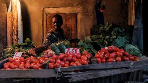 Getty Images A woman makes a selection of the most expensive tomatoes for a customer just before the 7PM curfew in Kibera, Nairobi on May 05, 2020.