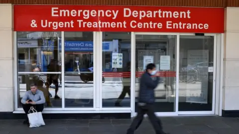 Getty Images A man wearing a protective face mask walks past the Emergency Department and Urgent Treatment Centre entrance to Chelsea and Westminster hospital in central London, March 23, 2020,