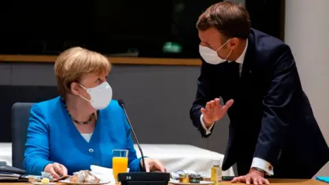 Getty Images Germany's Chancellor Angela Merkel (L) talks with France's President Emmanuel Macron prior the start of the EU summit at the European Council building in Brussels, on July 18, 2020