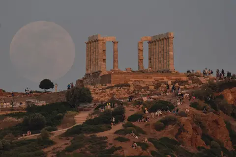 Louisa Gouliamaki / AFP Locals and tourists watch the moon rising by the Temple of Poseidon at the cape of Sounion, south of Athens, Greece