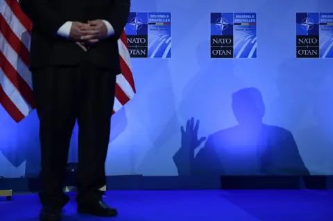  Brendan Smialowski / AFP US Secretary of State Mike Pompeo (left) looks on as US President Donald Trump casts a shadow as he addresses a press conference on the second day of the North Atlantic Treaty Organization (NATO) summit in Brussels