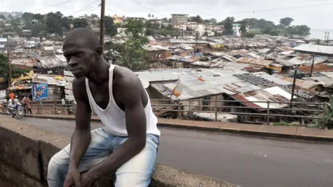 AFP An unidentified man sits on a wall in a township in Freetown on September 20, 2009 where Amnesty International Secretary-General Irene Khan (unseen) is campaigning to fight infant mortality -- one of the highest rates in the world