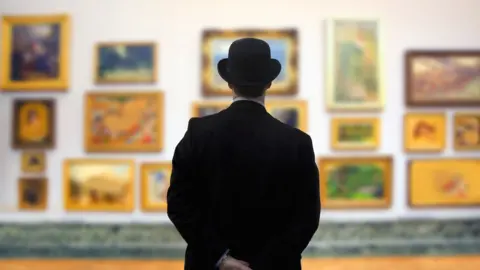 Getty Images A man in a bowler hat surveys a gallery wall with his hands behind his back