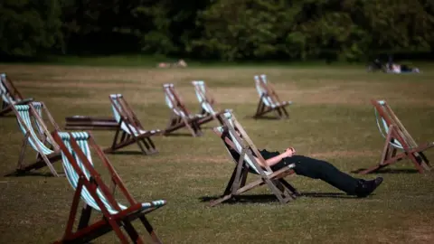 Getty Images A picture of a number of sun loungers on a warm day. A man is sitting in one of them.